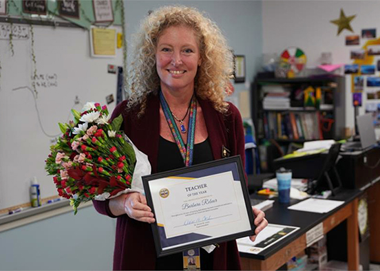 Blond woman standing in classroom holding flowers and a certificate