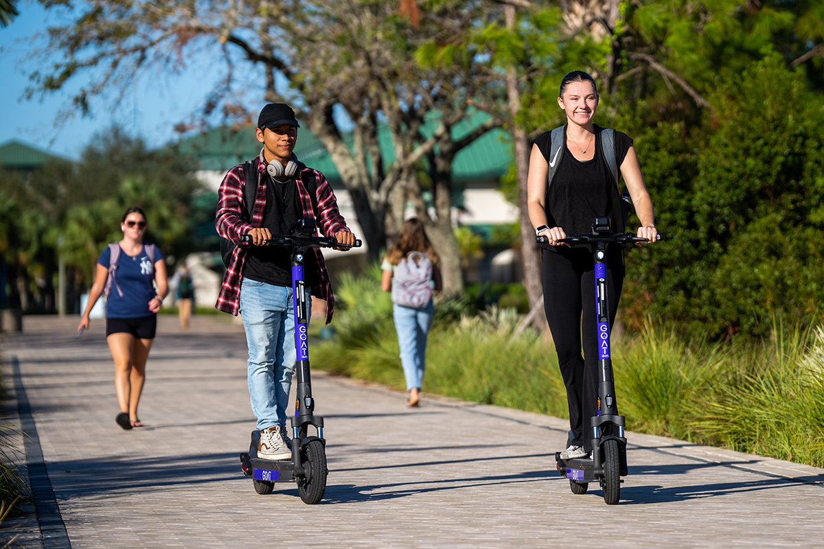 Man and woman riding scooters on FGCU campus