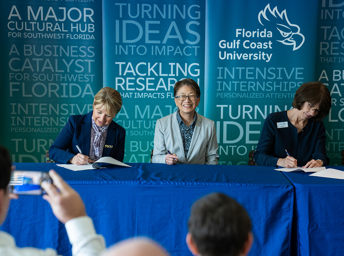 Three women sitting at table signing an agreement